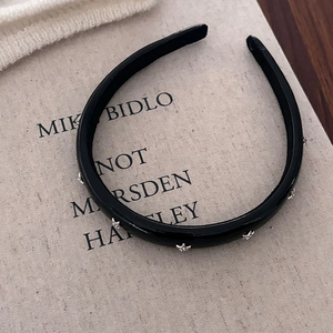 Minimalist black headband with silver star metal studs on artistic linen background