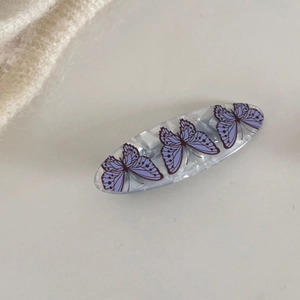 Dettaglio molletta in acrilico bianco con decorazioni a farfalla viola su sfondo beige
