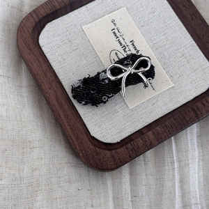 Close-up of black tweed hair clip with a silver metal bow and shiny sequins detail