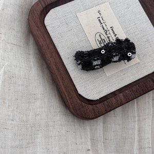 Detailed view of black denim hair clip with frayed edges and silver sequins on wooden tray