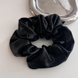 Elegant black pleated scrunchie with metallic sheen on minimalist silver metal tray