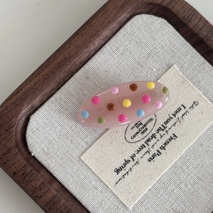 Detailed close-up of a pink resin hair clip with colorful polka dots on a wooden tray