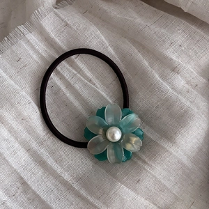 Detailed macro view of acetate flower hair tie with central pearl on fabric background
