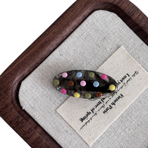 Oval marble resin hair clip with colorful 3D dots on a vintage linen card display