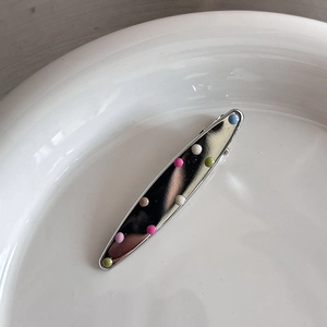 Gros plan d'une barrette argentée avec pois colorés sur une assiette en porcelaine