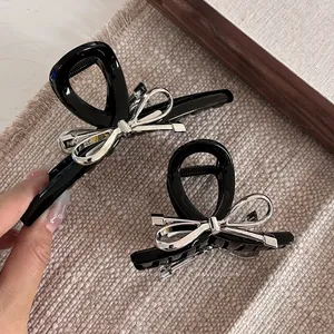Détail de pinces à cheveux en acrylique noir avec nœud métallique argenté sur tapis texturé