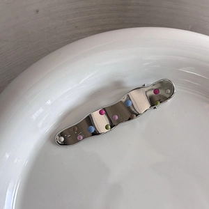 Détail d'une barrette à cheveux ondulée en métal argenté avec des points émaillés colorés