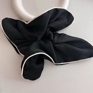 Detail of a large black scrunchie with white contrast piping on a white ceramic plate