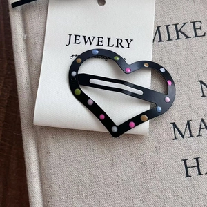 Black heart-shaped hair clip with colorful polka dots on jewelry display card