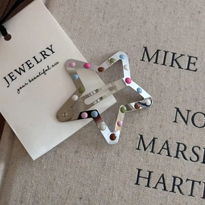 Detail of silver star metal hair clip with colorful dots on beige linen background