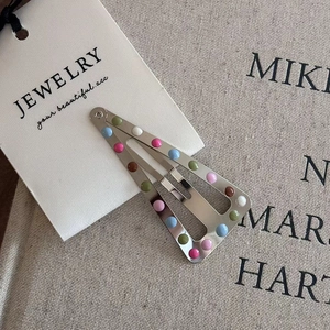 Close-up of a silver metal snap hair clip featuring colorful polka dots on a display card