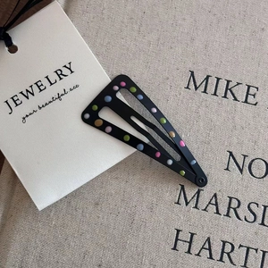 Detailed view of a black triangle hair clip with colorful dots on a textured fabric