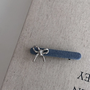 Barrette à cheveux en denim bleu avec nœud en métal argenté pour femme sur fond texturé