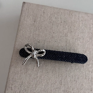 Détail d'une pince à cheveux en denim bleu avec un nœud en métal argenté poli