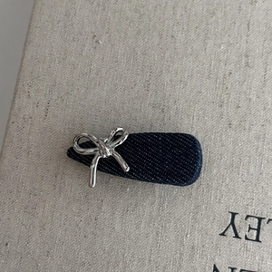 Détail d'une pince à cheveux en denim bleu avec nœud métallique argenté sur fond en lin