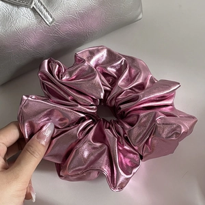 Detail of metallic pink scrunchie with shiny textured fabric held by a hand