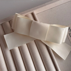 Elegant cream satin bow hair clip with long ribbons on a velvet display tray