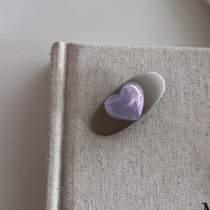 Close-up of a silver hair clip with a purple glittery heart on a textured book surface
