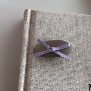 Minimalist silver ribbon hair clip with light purple cross bow on beige linen background