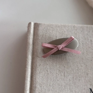 Elegant pink ribbon bow hair clip on a matte oval base clipped to a vintage linen book