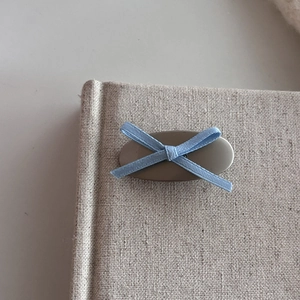 Detailed view of light blue ribbon bow hair clip on a minimalist matte metal base