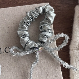Detail van een zilveren glitter bow scrunchie met strassteentjes op beige linnen