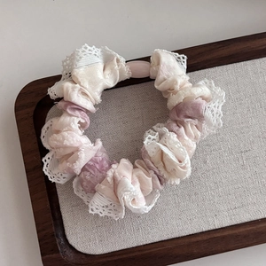 Pink tie-dye fabric scrunchie with lace edges and a pink pearl bead on a wooden tray