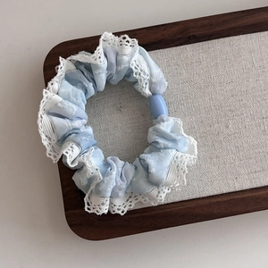 Light blue tie-dye fabric hair scrunchie with white lace trim and oval bead accent