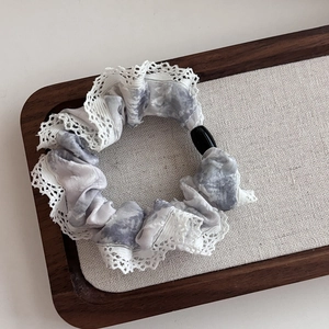 Floral tie-dye hair scrunchie with white lace trim and marble pattern in a wood tray