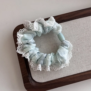 Close-up of light blue tie-dye scrunchie with white lace edges and resin charm