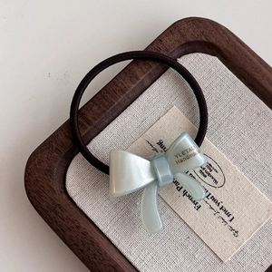 Elastic hair tie with light cyan acetate bow and gold label on wooden tray backdrop
