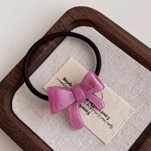 Detailed close-up of a pink acetate bow hair tie featuring golden handmade branding text