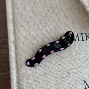 Détail d'une pince à cheveux noire ondulée à pois roses avec une finition brillante
