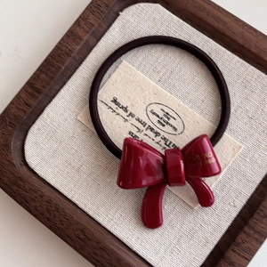 Detailed view of a red acetate bow hair tie with gold label on a rustic textured background