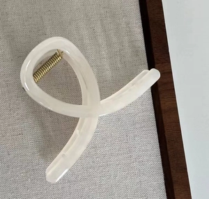 Nahaufnahme der beigen Haarspange mit goldener Metallfeder auf grauem Leinenhintergrund