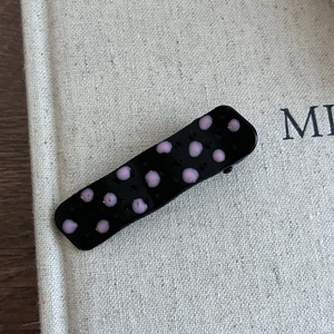 Détail d'une pince à cheveux noire à pois roses sur une surface en lin beige clair