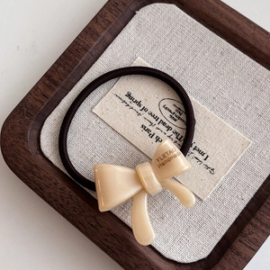 Detail of cream acetate bow hair tie with durable elastic band on wooden display tray