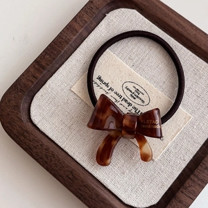 Detail of a handmade tortoiseshell acetate bow hair tie on a minimalist wooden tray