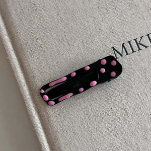 Détail d'une pince à cheveux noire en métal avec pois roses sur fond en lin beige