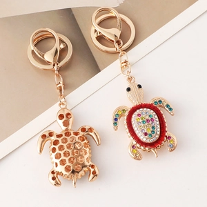 Porte-clés tortue dorée avec strass colorés et fermoir mousqueton sur fond blanc épuré