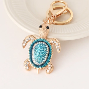 Porte-clés tortue dorée avec strass bleus sur une assiette en céramique blanche élégante