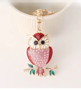 Close-up of golden owl keychain with red enamel wings and pink rhinestones detail
