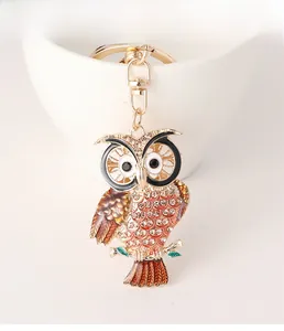 Close-up of golden owl keychain with colorful rhinestones and red enamel on a white cup