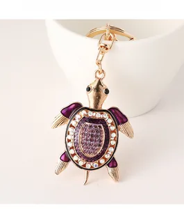 Détail d'un porte-clés tortue avec émail violet et strass accroché à une tasse blanche