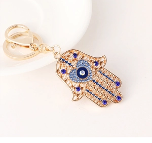 Détail du porte-clés main de Fatma dorée avec strass bleus et breloque œil porte-bonheur