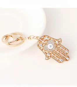 Détail du porte-clés Hamsa doré avec strass blancs et breloque oeil bleu en coeur
