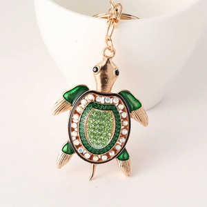 Porte-clés tortue dorée avec émail vert et strass posé sur une tasse en céramique blanche