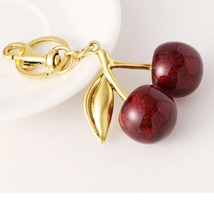 Detailed close-up of dark red glittery cherry keychain with golden leaves and lobster clasp