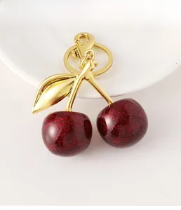 Detailed macro of red glitter resin cherry keychain with golden leaf and lobster clasp