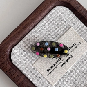Translucent smoky grey oval hair clip with colorful polka dots on a rustic background